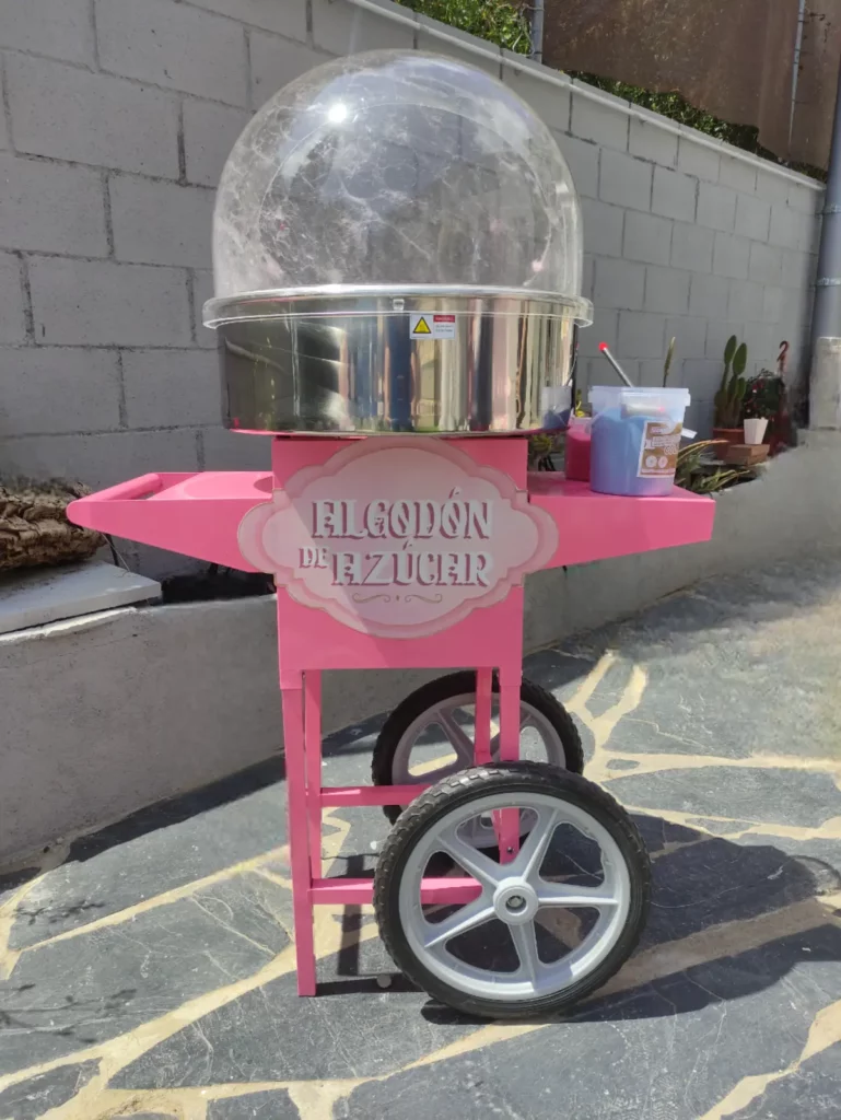 Carrito de algodón de azúcar de color rosita, con dos ruedas negras, tirador para llevar una pequeña mesita de trabajo.
